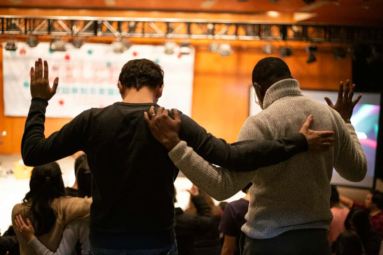 Two friends praying together, arms around each other's shoulders